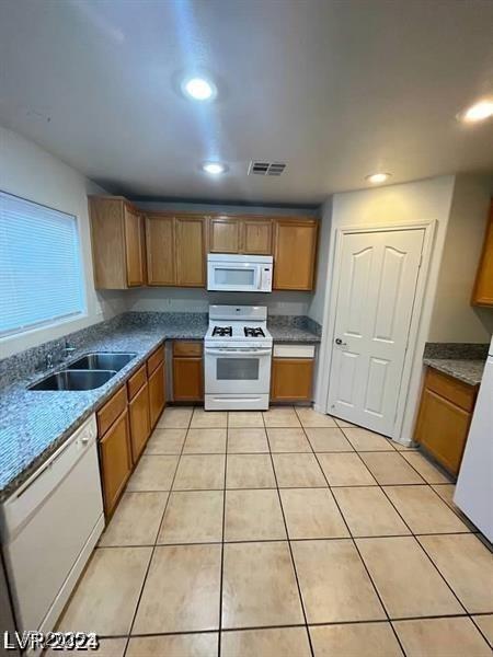 kitchen with light tile patterned floors, white appliances, a sink, visible vents, and brown cabinetry