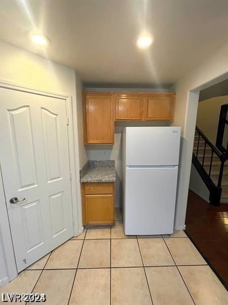 kitchen with light tile patterned floors, brown cabinets, and freestanding refrigerator