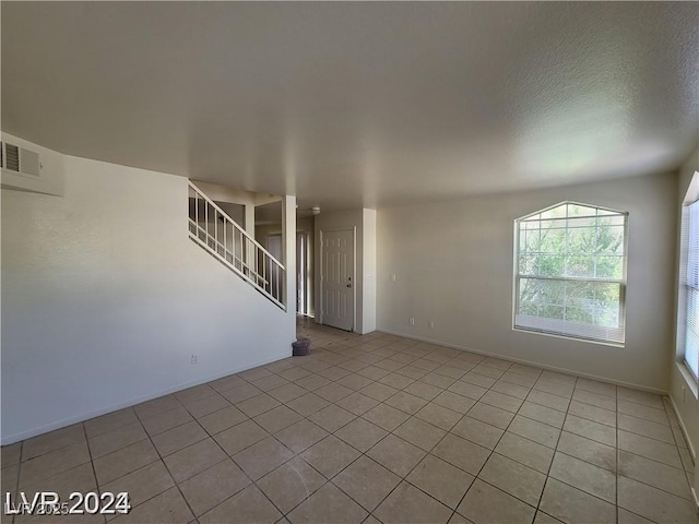 spare room with light tile patterned floors, baseboards, visible vents, stairway, and a textured ceiling