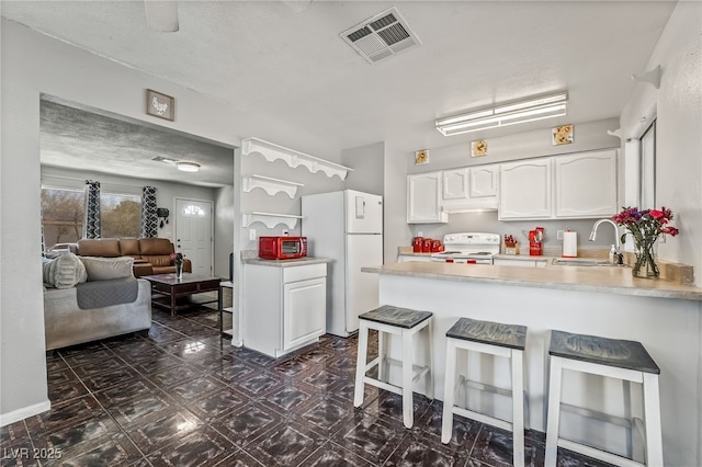 kitchen with visible vents, a sink, white appliances, a peninsula, and white cabinets