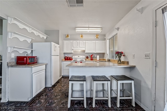 kitchen with visible vents, a sink, white appliances, a peninsula, and white cabinets