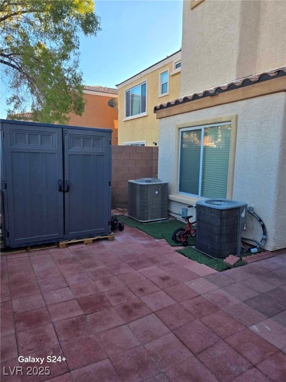 view of patio with an outbuilding, fence, a shed, and central air condition unit