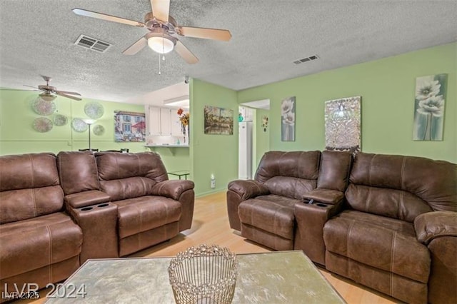 living room featuring light wood-style floors, ceiling fan, visible vents, and a textured ceiling