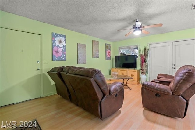 living area featuring light wood-style floors, ceiling fan, visible vents, and a textured ceiling