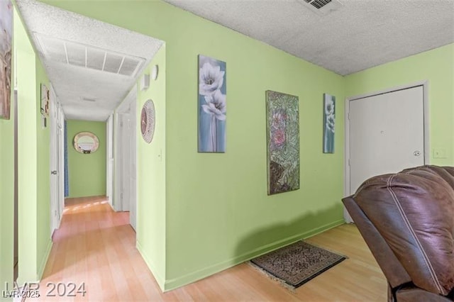 corridor with baseboards, light wood-style flooring, visible vents, and a textured ceiling