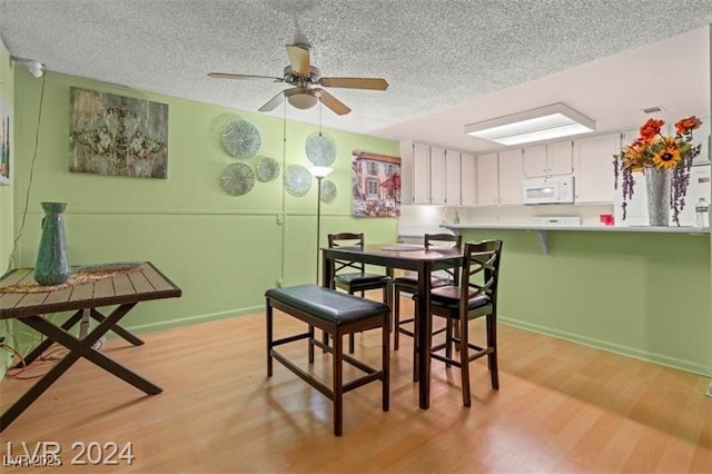 dining area featuring light wood-type flooring, ceiling fan, baseboards, and a textured ceiling