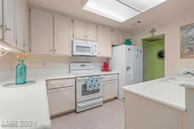 kitchen with white appliances, a sink, visible vents, white cabinetry, and light countertops