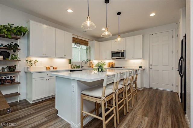 kitchen featuring a kitchen island, stainless steel microwave, white cabinets, and light countertops