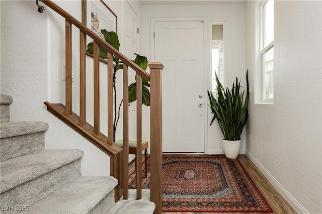 entryway featuring stairs, a textured wall, baseboards, and wood finished floors