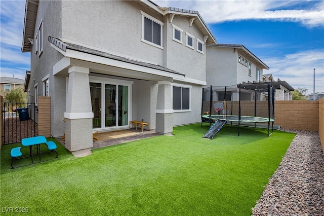 back of house with a fenced backyard, a trampoline, and stucco siding