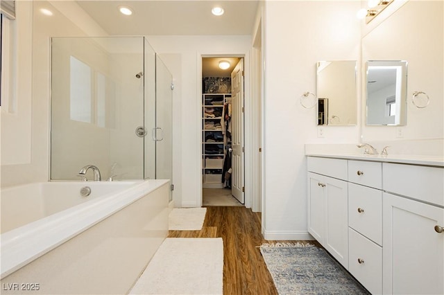 bathroom featuring recessed lighting, a spacious closet, a shower stall, wood finished floors, and a bath