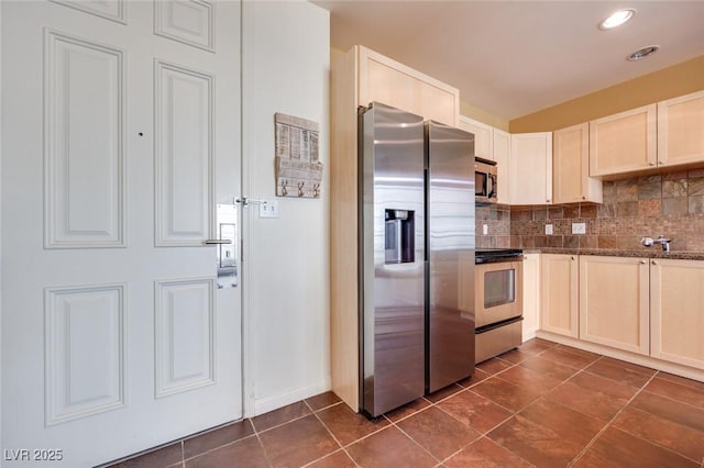 kitchen with appliances with stainless steel finishes, decorative backsplash, dark stone countertops, and dark tile patterned flooring