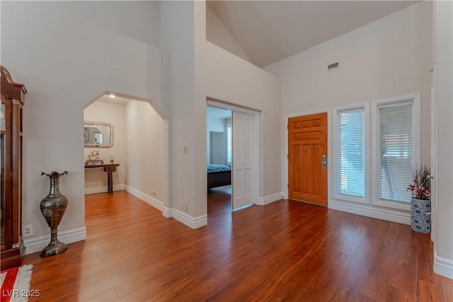 entrance foyer with baseboards, visible vents, arched walkways, wood finished floors, and high vaulted ceiling