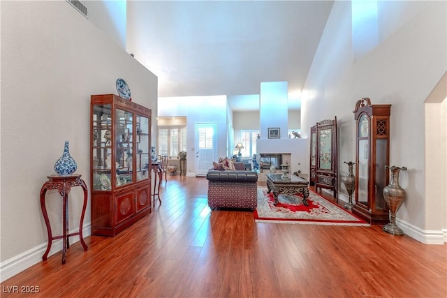 living room featuring baseboards, visible vents, a high ceiling, and wood finished floors