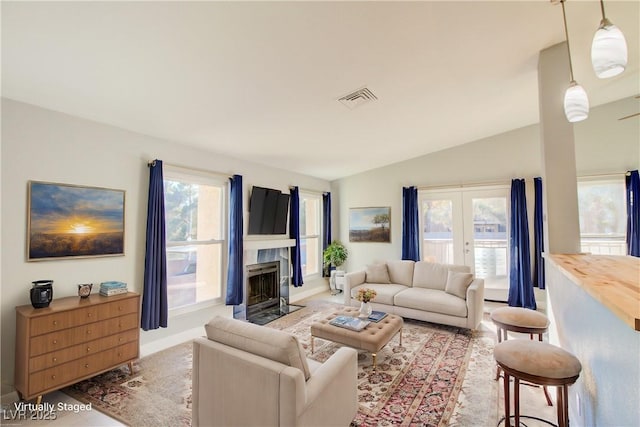 living area with a fireplace with flush hearth, french doors, visible vents, and vaulted ceiling