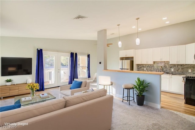 living room with lofted ceiling, light carpet, visible vents, baseboards, and french doors