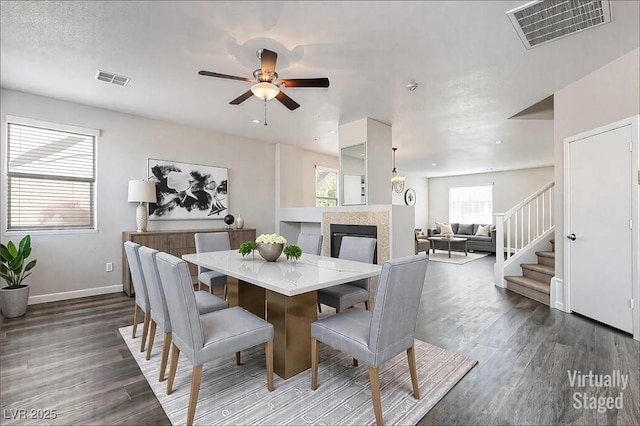 dining room with dark wood-style floors, stairs, visible vents, and a multi sided fireplace