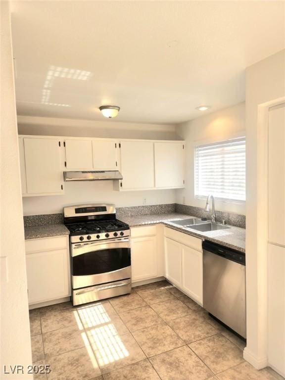 kitchen with stainless steel appliances, dark countertops, white cabinets, a sink, and under cabinet range hood