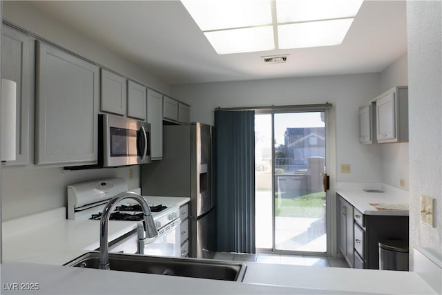 kitchen featuring light countertops, stainless steel microwave, a sink, and visible vents