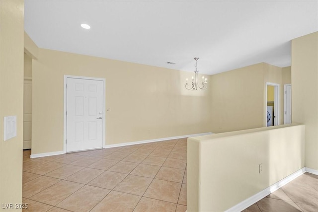 empty room with washer / dryer, a chandelier, baseboards, and light tile patterned floors