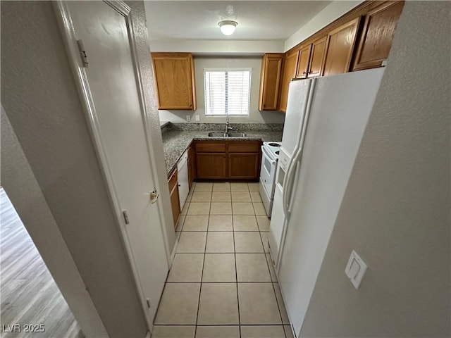 kitchen featuring brown cabinetry, white appliances, light tile patterned flooring, and a sink