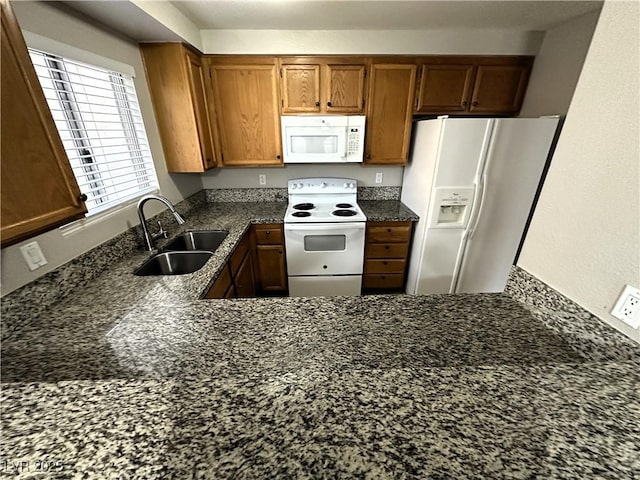 kitchen with dark stone counters, white appliances, a sink, and brown cabinets