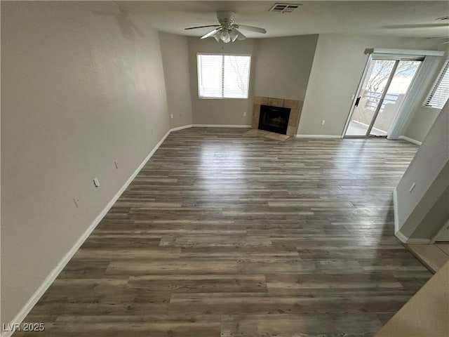 unfurnished living room with baseboards, visible vents, a ceiling fan, a tile fireplace, and dark wood-type flooring