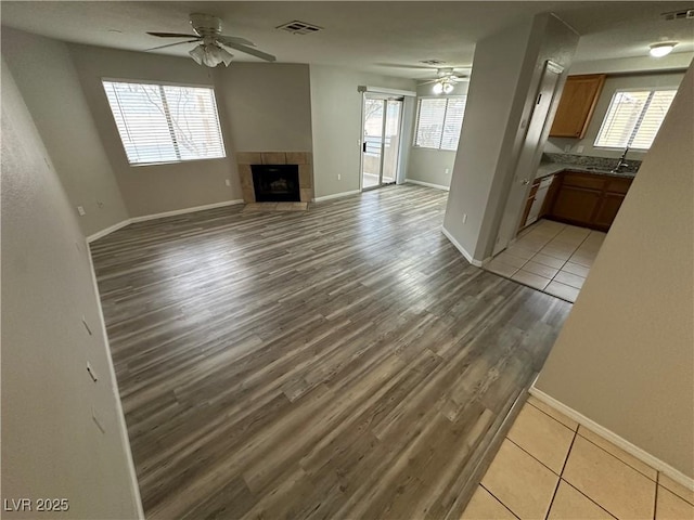 unfurnished living room with ceiling fan, a tile fireplace, visible vents, baseboards, and light wood finished floors