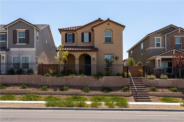 mediterranean / spanish-style house with stairway, a tile roof, a fenced front yard, and stucco siding