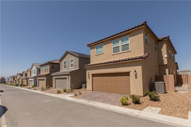 mediterranean / spanish home featuring an attached garage, cooling unit, a residential view, and stucco siding