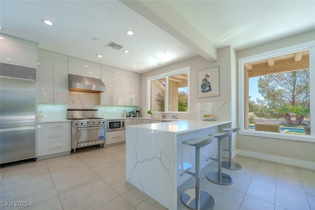 kitchen featuring light countertops, white cabinetry, wall chimney range hood, modern cabinets, and built in appliances