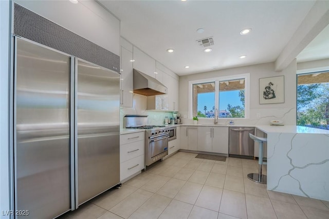 kitchen with built in appliances, visible vents, white cabinets, wall chimney range hood, and modern cabinets