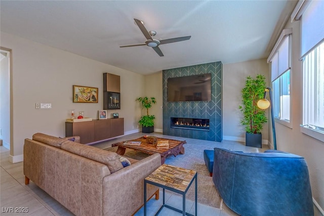 living area featuring a ceiling fan, baseboards, a tiled fireplace, and light tile patterned flooring