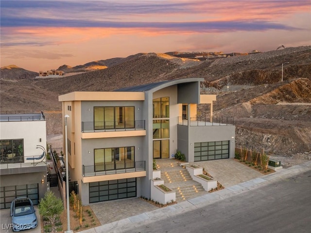 contemporary house featuring a garage, decorative driveway, a mountain view, and stucco siding