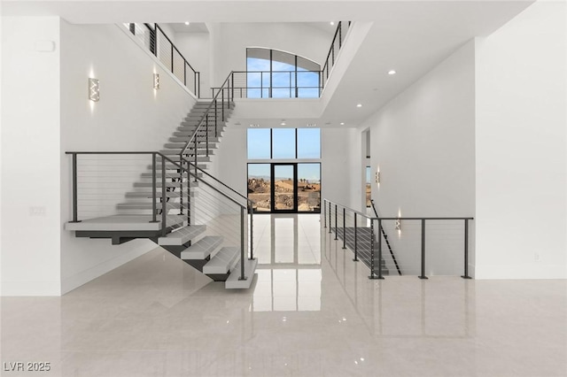 stairway featuring a healthy amount of sunlight, a towering ceiling, baseboards, and recessed lighting