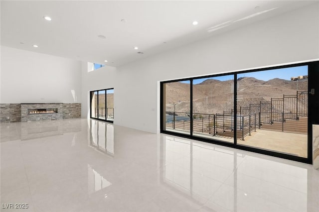 tiled empty room featuring a towering ceiling, recessed lighting, a mountain view, and a stone fireplace