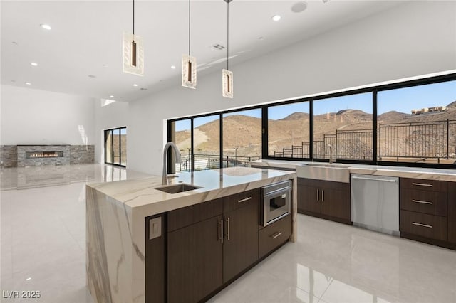 kitchen with a large island with sink, stainless steel dishwasher, a mountain view, pendant lighting, and a sink