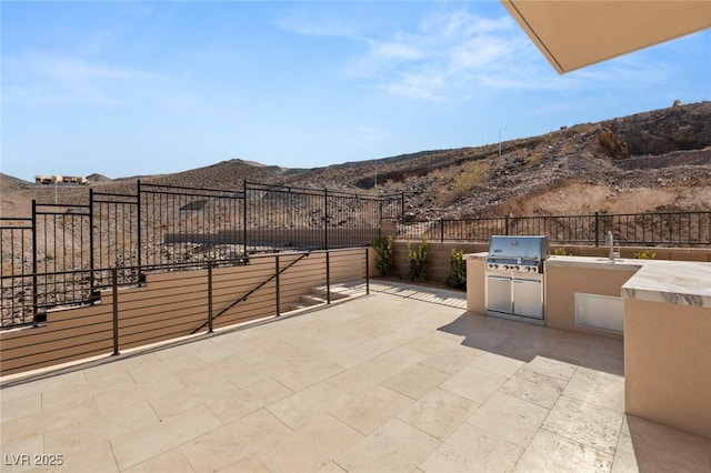 view of patio with exterior kitchen, fence, grilling area, and a mountain view