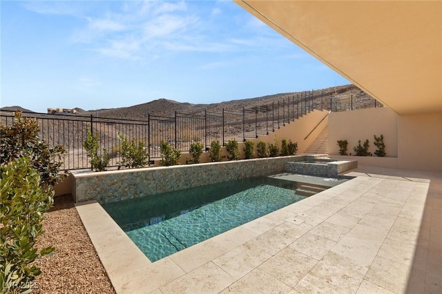 view of swimming pool with a pool with connected hot tub, fence, a mountain view, and a patio