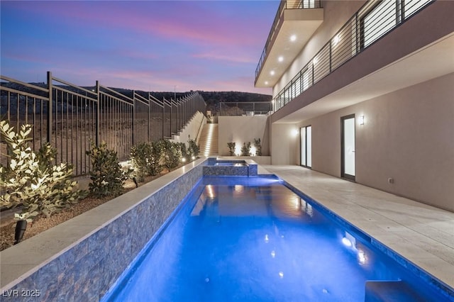 pool at dusk featuring a patio, a fenced backyard, and a pool with connected hot tub