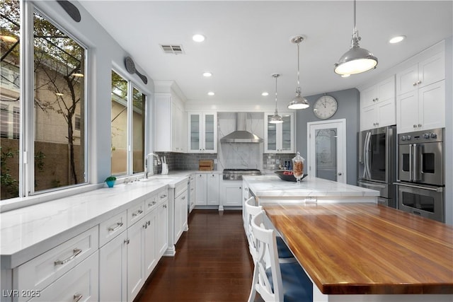 kitchen featuring white cabinets, wall chimney exhaust hood, glass insert cabinets, and a center island