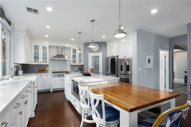 kitchen with a center island, glass insert cabinets, appliances with stainless steel finishes, white cabinets, and wall chimney range hood