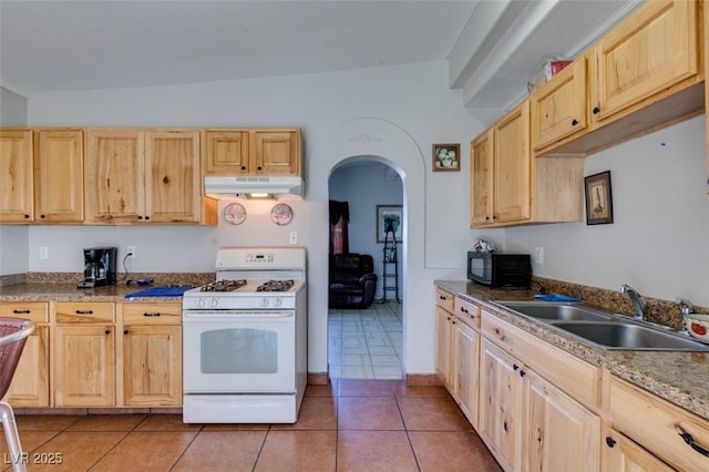 kitchen featuring white gas range oven, under cabinet range hood, light brown cabinets, black microwave, and a sink