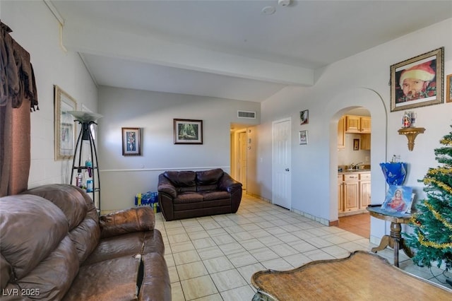 living area featuring baseboards, visible vents, arched walkways, vaulted ceiling with beams, and light tile patterned flooring