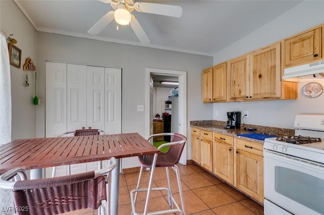 kitchen featuring light tile patterned floors, dark countertops, white gas range, under cabinet range hood, and light brown cabinets