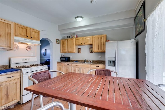 kitchen with under cabinet range hood, stainless steel refrigerator with ice dispenser, light brown cabinets, and white range with gas cooktop