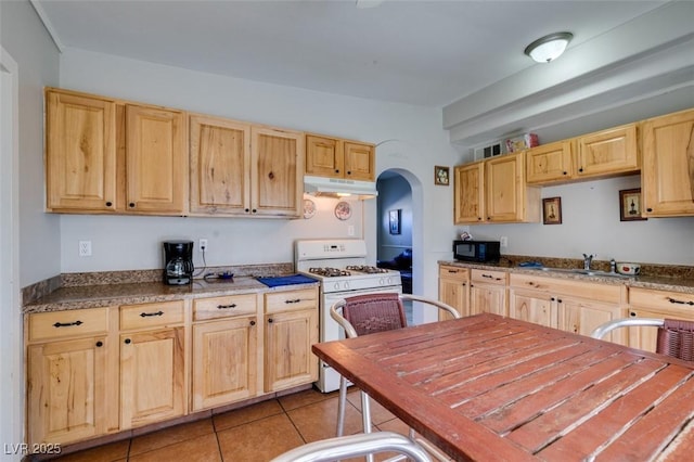 kitchen featuring arched walkways, gas range gas stove, light brown cabinetry, black microwave, and under cabinet range hood