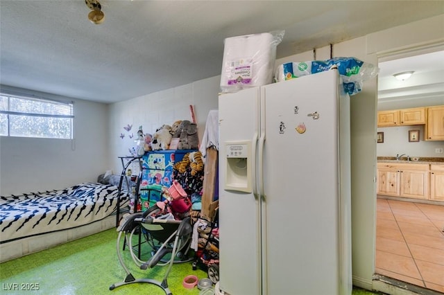 bedroom with a textured ceiling, white fridge with ice dispenser, light tile patterned flooring, and a sink