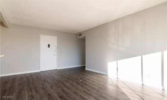 spare room featuring baseboards, visible vents, and dark wood finished floors