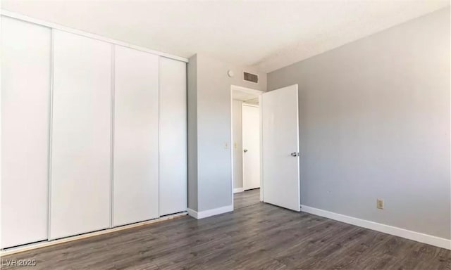 unfurnished bedroom featuring a closet, dark wood finished floors, visible vents, and baseboards